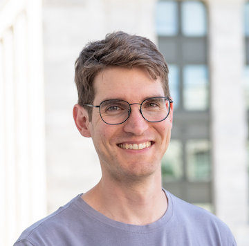 A white man with short, brown hair and glasses, smiling