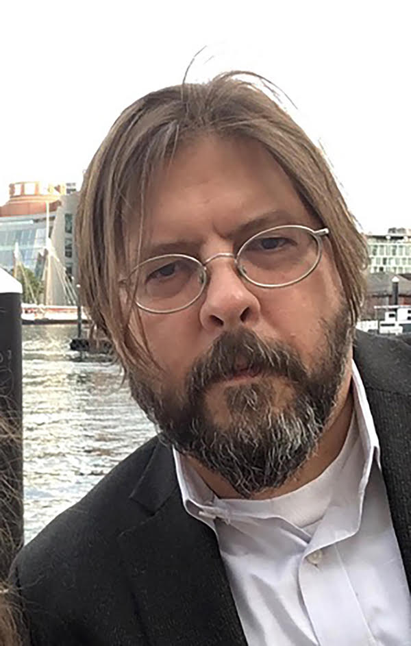 A man with blond-brown hair and a beard, with glasses