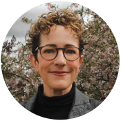 A woman with curly brown and highlighted short hair and glasses
